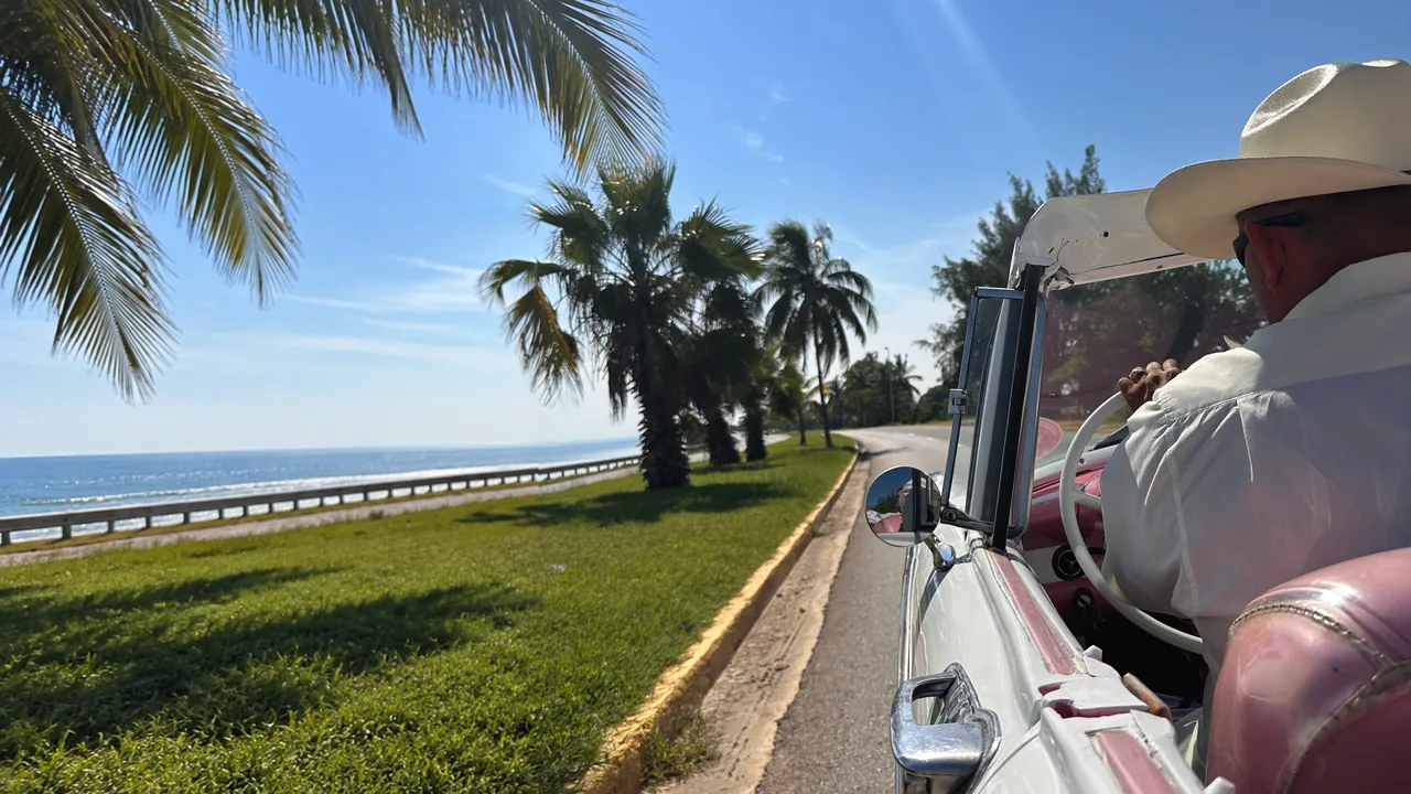 Fahrt im Oldtimer-Cabrio auf Kuba, am Steuer ein Fahrer mit Hut